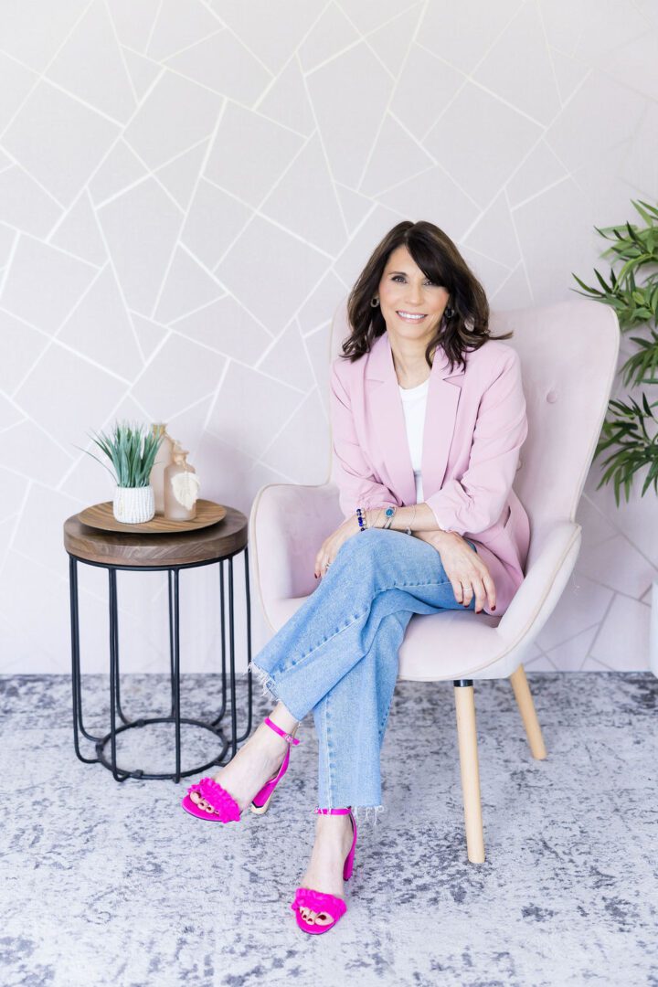 Woman sitting on chair, wearing pink blazer.