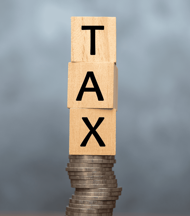 Wooden blocks spelling TAX on stacked coins.