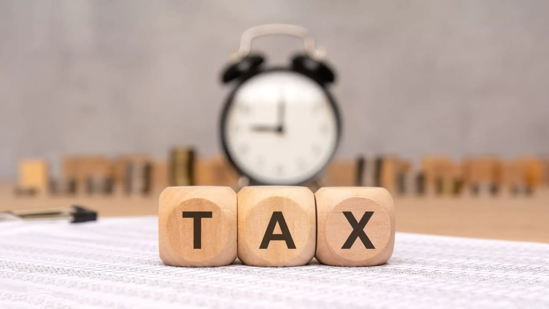Wooden blocks spelling TAX with a clock in the background.